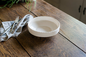 The coupe is a low bowl perfect for pasta, a salad, or anything saucy, with an elegant lip and a scalloped edge inspired by ceramics found in archaeological digs at the Historic 1747 Parsonage in Germantown, New York. White porcelain pasta bowl with silver flatware and linen napkin.