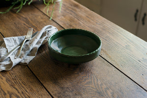 The coupe is a low bowl perfect for pasta, a salad, or anything saucy, with an elegant lip and a scalloped edge inspired by ceramics found in archaeological digs at the Historic 1747 Parsonage in Germantown, New York. Mugwort dark forest green with linen napkin