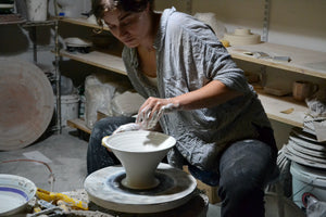 Hand-thrown shade in semi-translucent porcelain glows softly when illuminated, revealing the hand of the maker. Cast porcelain base and brass body. Touch switch. Designed and made in our workshop in the Hudson Valley. Aleah shown throwing a library lamp shade in the ceramics production studio. Quittner. 