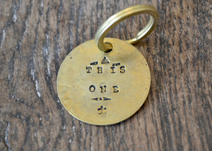 A solid brass key tag hand stamped in our workshop with “This One". Each piece is one-of-a-kind and comes on a brass key ring.