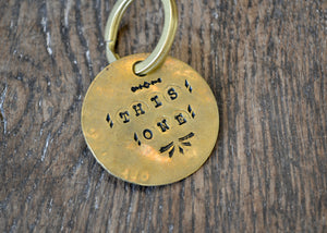 A solid brass key tag hand stamped in our workshop with “This One". Each piece is one-of-a-kind and comes on a brass key ring.