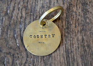 A solid brass key tag hand stamped in our workshop with “Country". Each piece is one-of-a-kind and comes on a brass key ring.