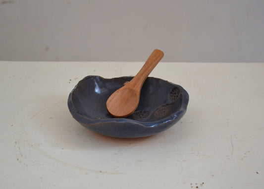 Dark blue ceramic bowl with a wooden spoon on a white surface