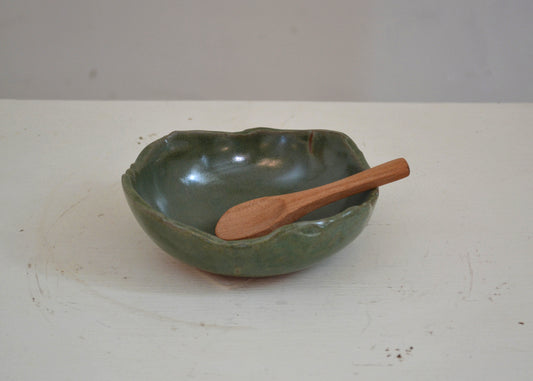 Green ceramic bowl with a wooden spoon on a white surface
