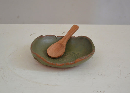 Green ceramic dish with a wooden spoon on a white surface