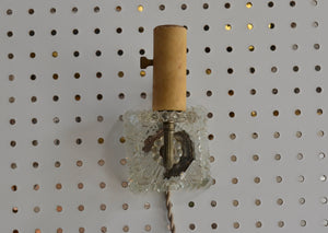 a vintage glass plug-in sconce that is to be hung on the wall off of a screw, nail, or hook. It is operated with a switch on the socket, and has a 6 foot long cloth-covered cord. It was previously damaged, and a former owner added the metal bracket for hanging.