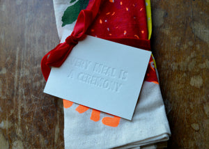 Note with 'Every meal is a ceremony' text on a colorful fabric background of folded napkins