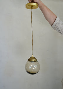 Hand holding a pendant light with a glass bulb and brass fixture against a plain background