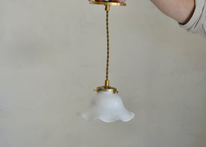 Antique glass pendant with a scalloped form. Cast brass shade holder and brass hardware. Cloth-covered cord. Ideal for over a kitchen or pantry sink, or in a laundry or powder room. Quittner.