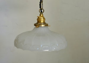 Vintage-style pendant light with white glass shade and brass fitting against a plain background