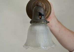Hand adjusting a restored antique wall light fixture with a glass shade.