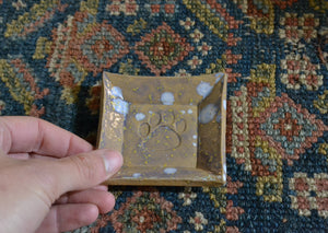 This is a small snack plate for your desk, ring dish for your bedside table, or landing zone for a wet tea bag. Use it for whatever needs a small spot to rest. Stamped with a paw print and glazed with speckles. Quittner. Hudson Valley Made by Lara Gillett. 