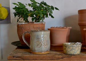 This large 16oz mug was handmade by potter Lara Gillett using slab-building techniques. It features a horse stamp with a creamy glaze. Each mug is made by hand and there will be variation in exact form and glaze. Such variations are inherent to the material and process. Quittner. Lara Gillett. Hudson Valley.