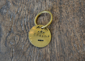 A solid brass key tag hand stamped in our workshop with “Country". Each piece is one-of-a-kind and comes on a brass key ring.