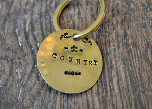 A solid brass key tag hand stamped in our workshop with “Country". Each piece is one-of-a-kind and comes on a brass key ring.