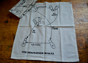 Natural cotton napkin with diagram and text 'The Hesitation Waltz' on a wooden surface