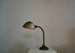 Vintage desk lamp on a white pedestal against a plain wall. Quittner.