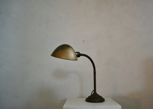 Vintage desk lamp on a white pedestal against a plain wall. Quittner.