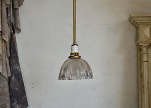 This is a pendant light on a fixed-length brass pipe featuring a vintage holophane glass shade, porcelain socket, brass details, offering a warm glow with a bit of sparkle. Rewired. Vintage glass has some small nicks and chips, so please look carefully at images to confirm condition. Quittner.