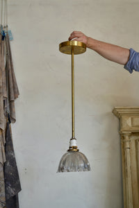 This is a pendant light on a fixed-length brass pipe featuring a vintage holophane glass shade, porcelain socket, brass details, offering a warm glow with a bit of sparkle. Rewired. Vintage glass has some small nicks and chips, so please look carefully at images to confirm condition. Quittner.