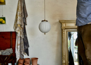 Art Deco-era vintage pendant light featuring a ribbed frosted glass orb and brass details, offering a warm glow. Rewired. Quittner.