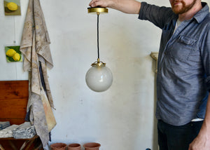 Pendant light featuring a vintage hand-blown frosted glass orb and brass details, offering a warm glow. Rewired. Please look carefully at images to confirm condition. Quittner.