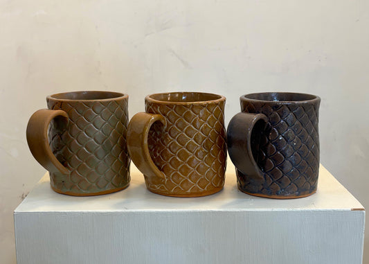 Three ceramic mugs with textured handles on a white surface against a light background