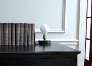 Designed to be a clean and elegant addition to a nightstand or reading nook, the Simple Lamp is just that — simple. A hand cast porcelain base anchors a brass socket with a natural living finish that will patina over time. Fitted with a touch sensor, you turn the Simple Lamp on or off by simply taping the brass socket with a finger. Quittner