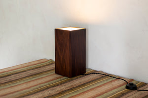 A canister-style floor lamp, or uplight, in black walnut with brass feet that offers a diffused upwards light. Designed and made in the Hudson Valley. Bedroom style, bedside table lamp, uplight, canister lamp, black walnut lamp, foot pedal, luxury home